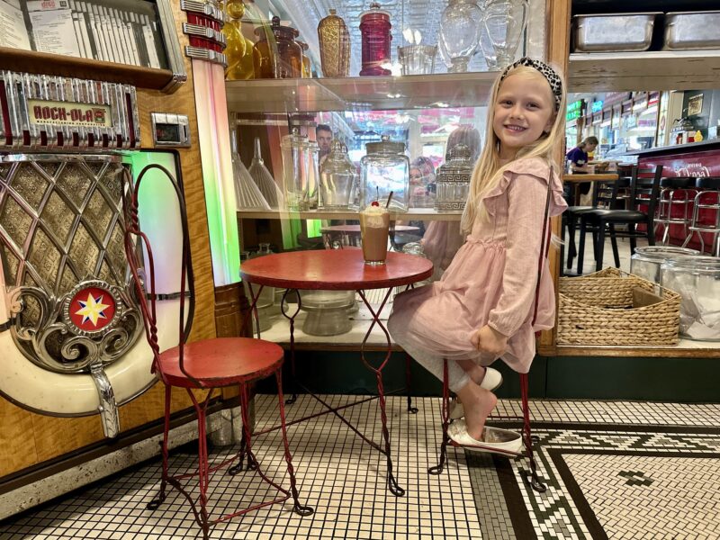 little girl sitting on a small table next to the jute box at Mikes on Main Hendersonville, NC