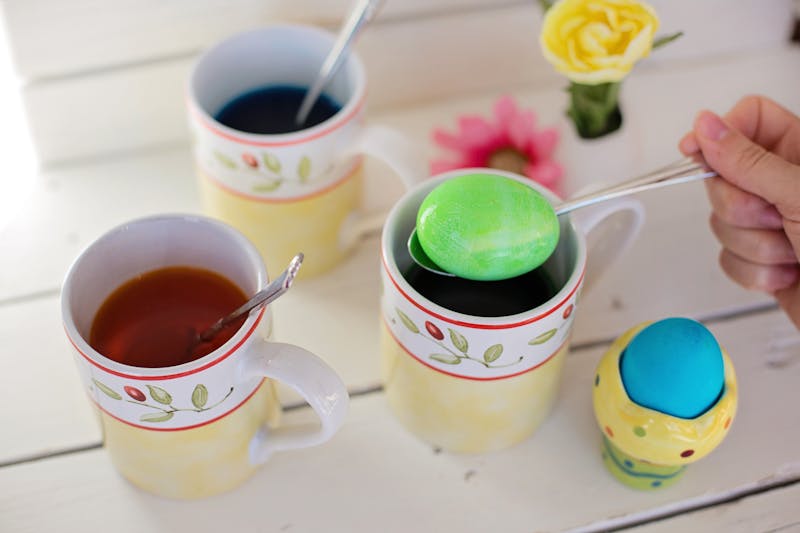 Vibrant Easter egg dyeing scene with mugs and colorful eggs on a wooden table.